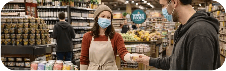 Masked brand ambassador handing a sample to a shopper in a grocery store during the pandemic.